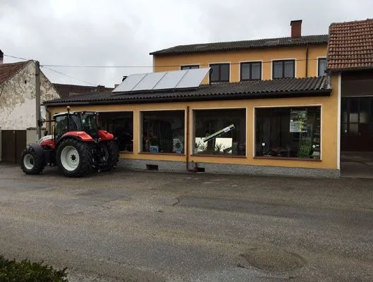 Ockerfarbenes Geschäft mit großen Fenstern, davor ein roter Steyr-Traktor