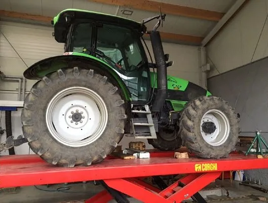 Grüner Traktor auf einer roten Hebebühne in der Werkstatt
