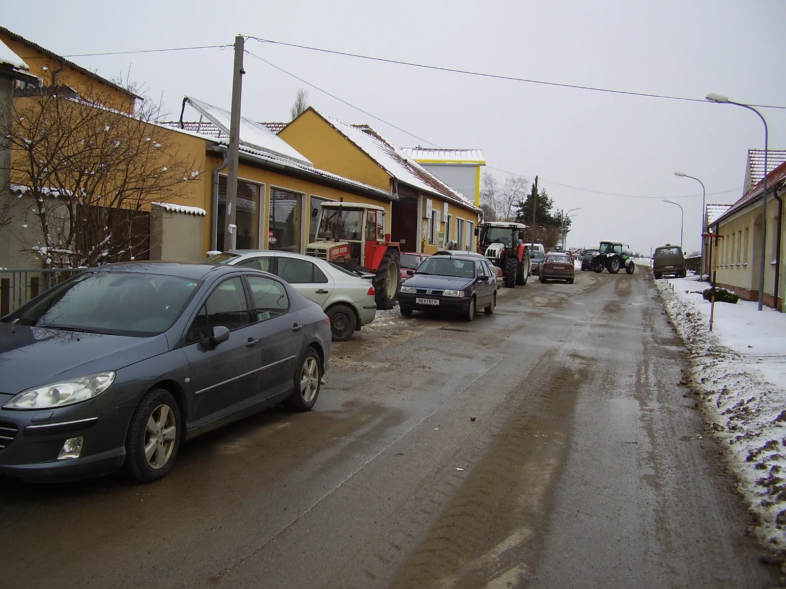 Dorfstraße vor dem Betrieb im Winter, am Straßenrand Autos und Traktoren