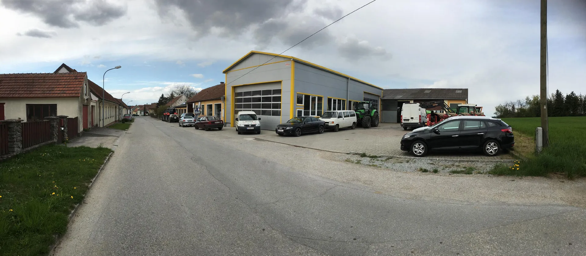 Gelbe Werkstatthalle der Firma Wolf an der Dorfstraße in Raisdorf, davor Autos und Traktoren